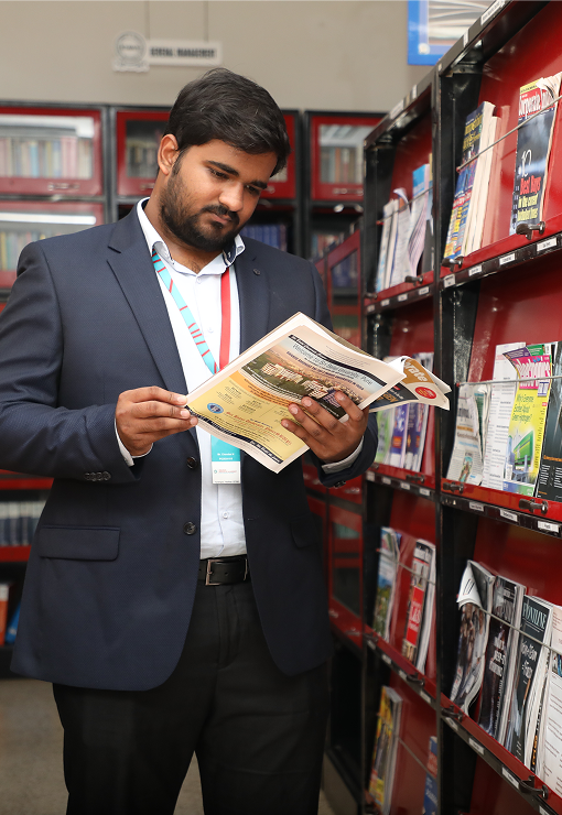 Student reading a book in the library aisle with bookshelves in the background at KIM Harihar