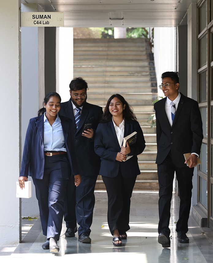 Students in formal attire walking through campus corridor holding books and laptop at Kirloskar Institute of Management harihar