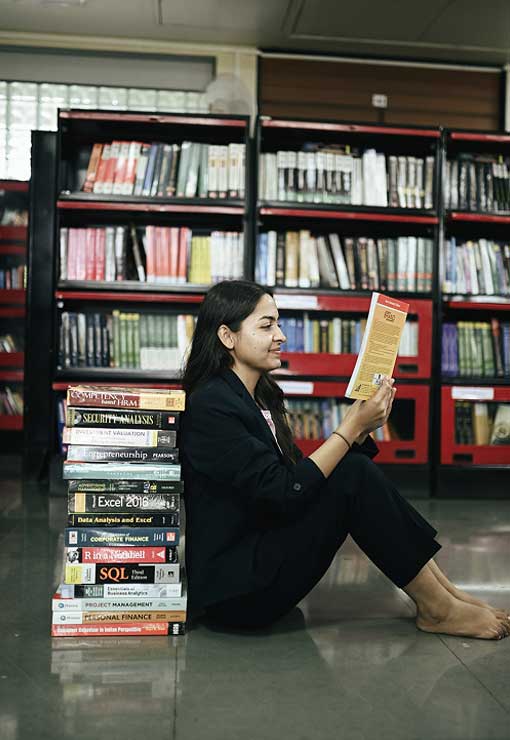 Mangement student sitting beside stack of books in the KIM Pune Campus library