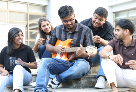 Student playing guitar while friends sit together on KIM Pune campus steps