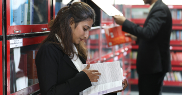 Student reading a book near library shelves at Kirloskar Institute of Management Pune
