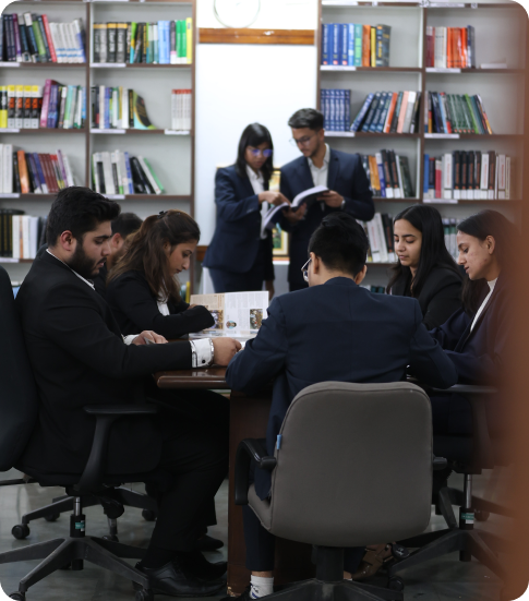 Students studying together at a library table with bookshelves in the background