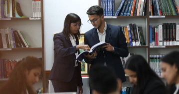 Faculty member guiding students while referring to a book in the library at KIM Pune